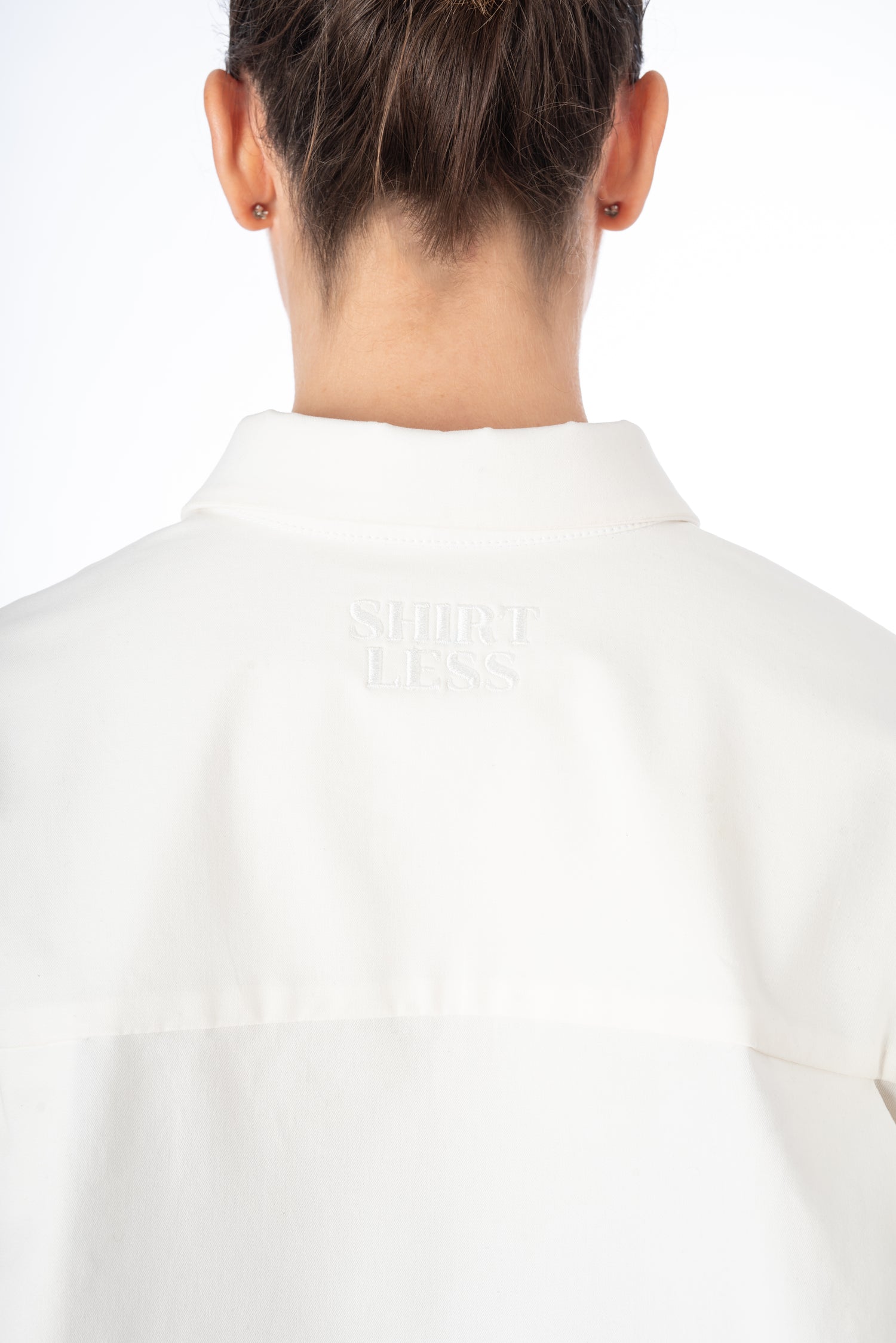 Close-up of the back of a white oversized shirt, featuring an embroidered logo next to the collar, showcasing meticulous craftsmanship.