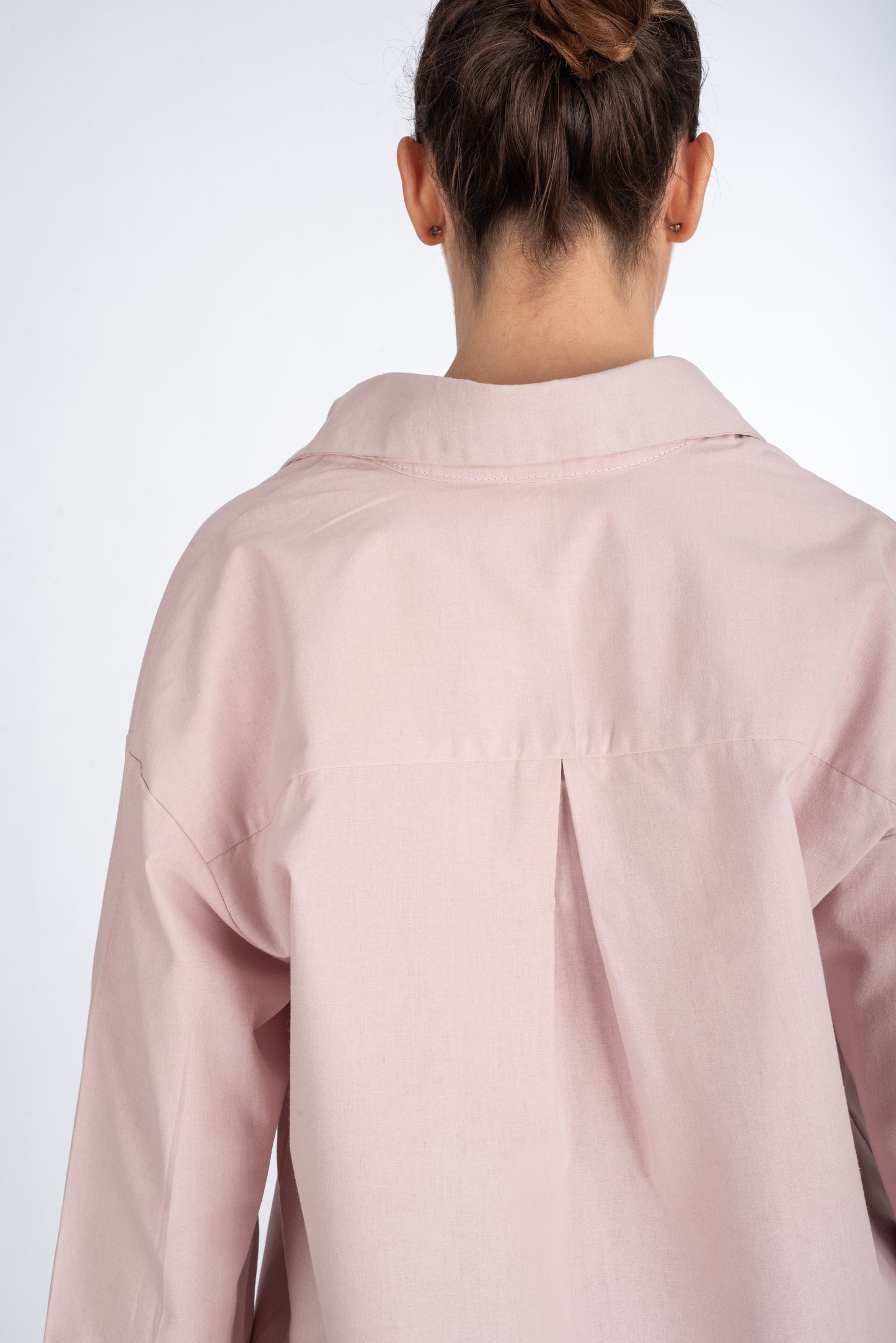 Lifestyle shot of the back of a dusty pink women's shirt, highlighting the center pleat at the yoke and sleek, minimal design.