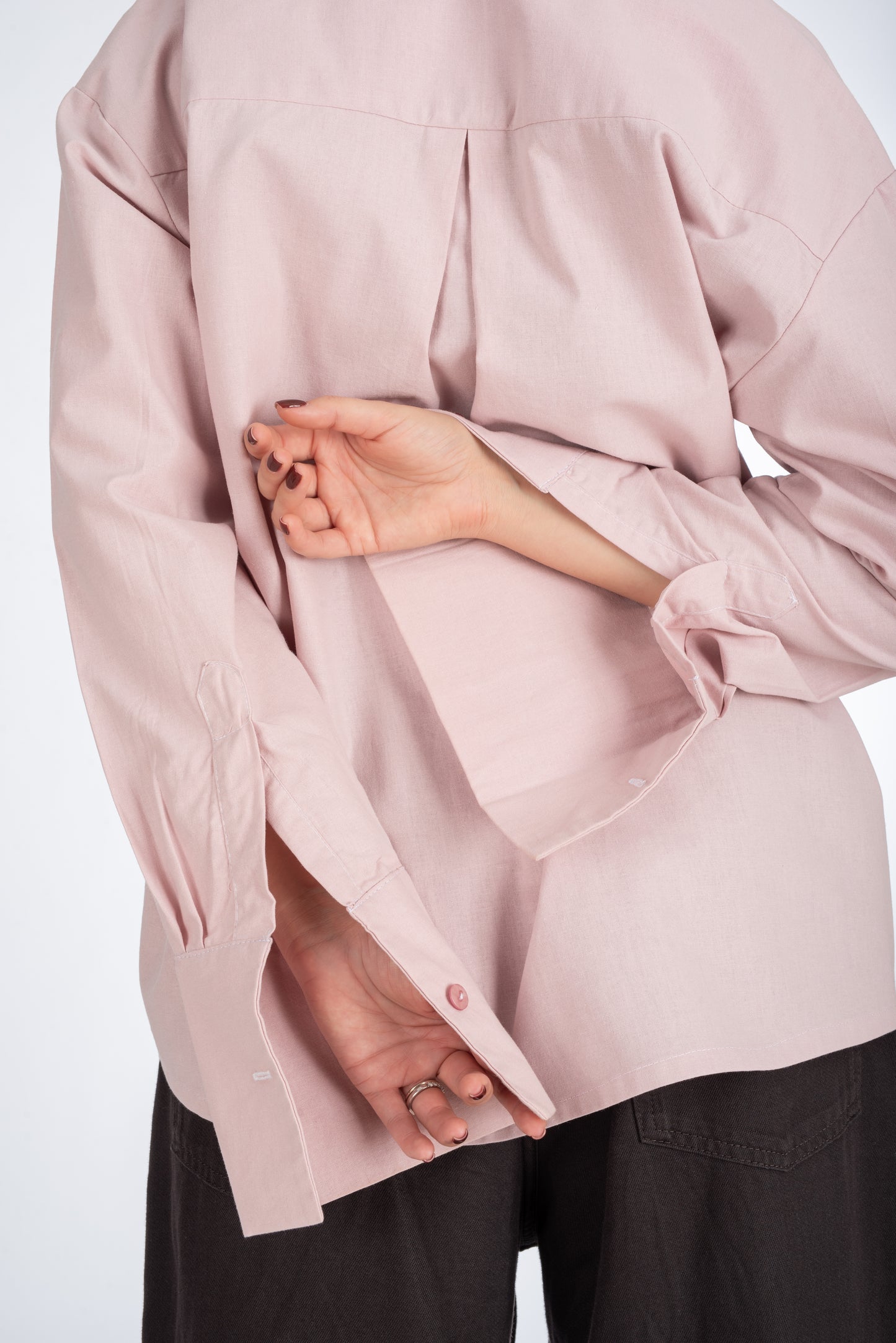 Lifestyle shot of the back of a dusty pink women's shirt, highlighting the center pleat at the yoke and sleek, minimal design.