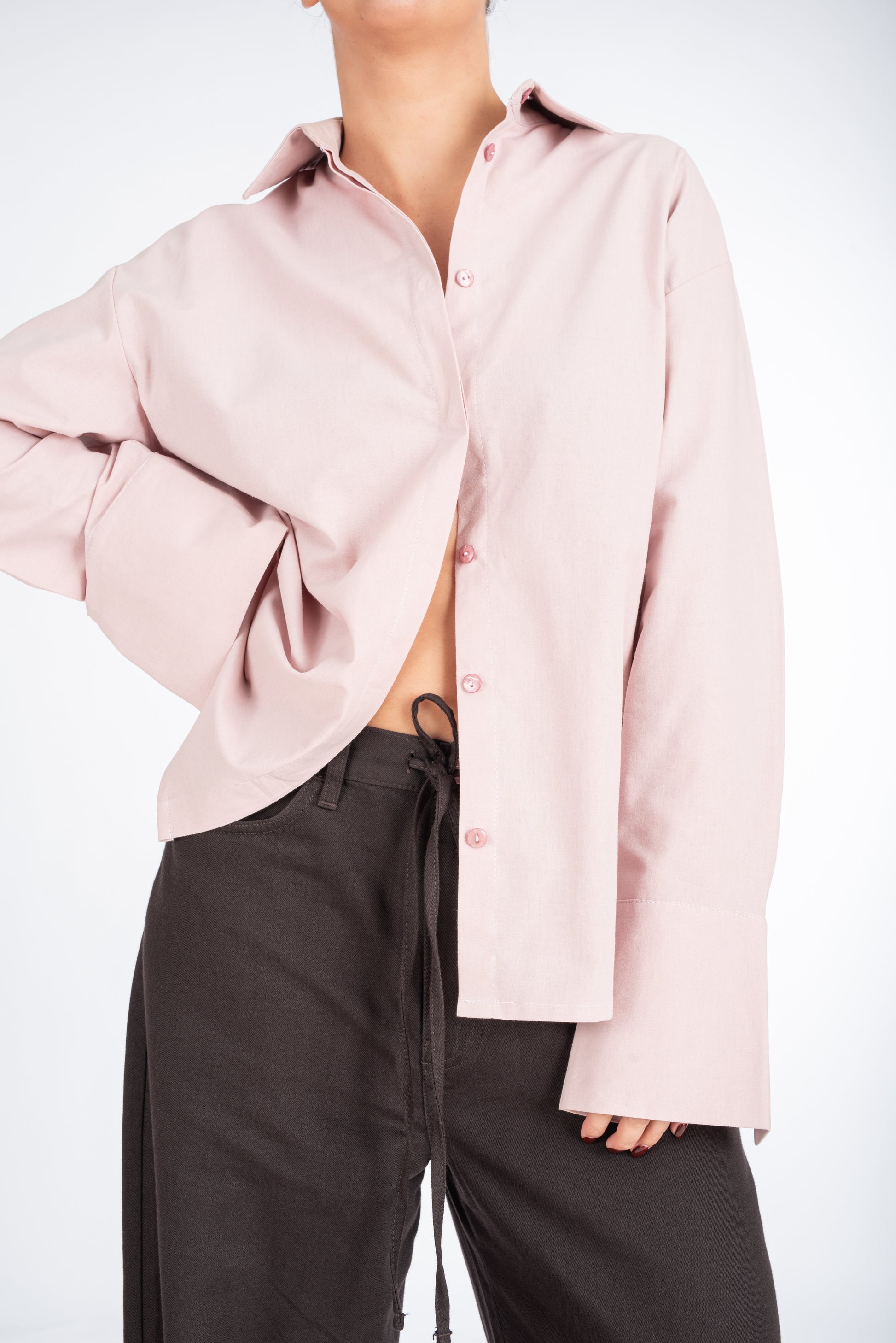 Lifestyle image of a woman wearing a dusty pink straight-fit shirt, featuring a minimalist collar and hidden placket for a modern, polished look.