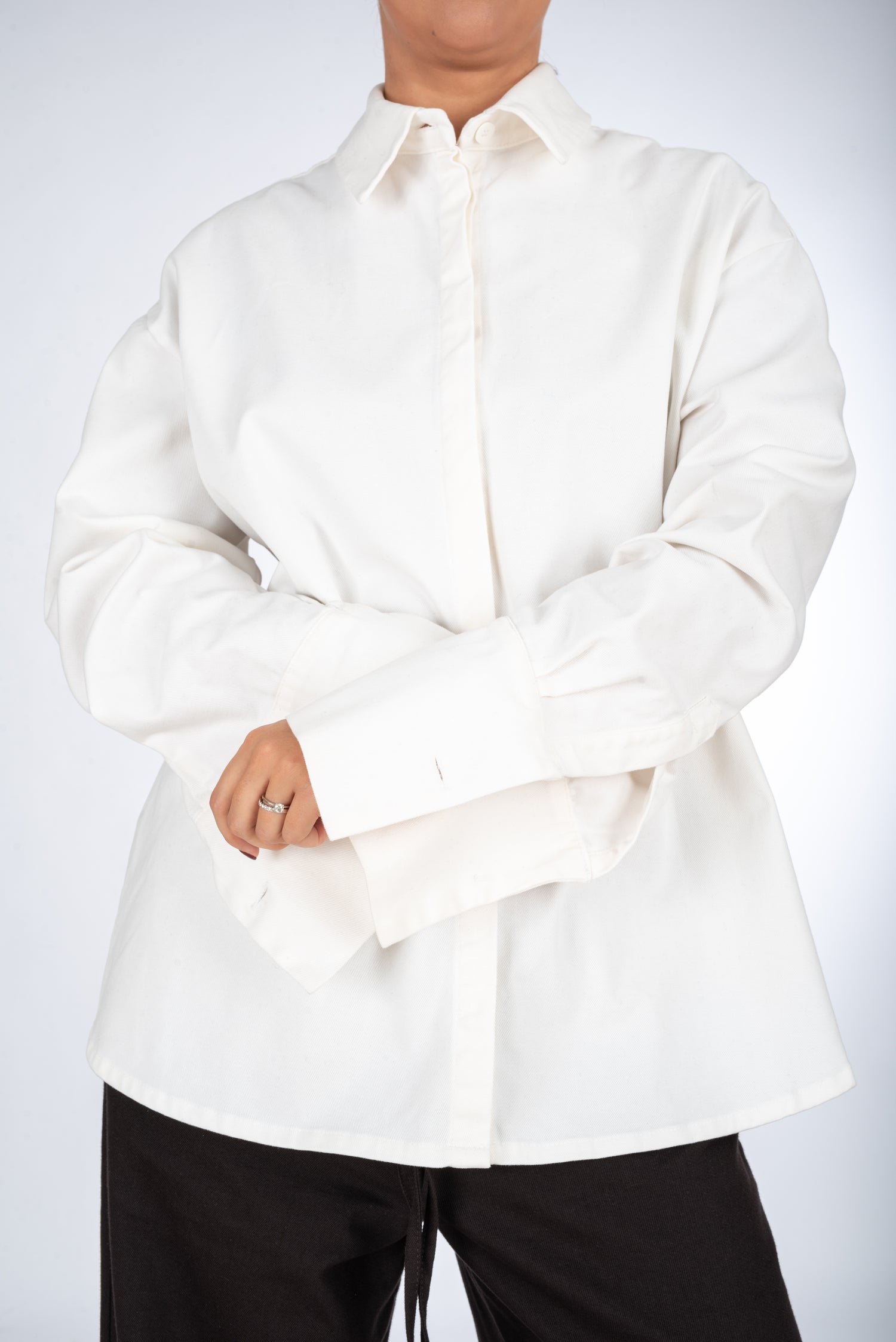 Lifestyle image of a woman wearing a thick high quality white straight-fit shirt, featuring a minimalist collar and hidden placket for a modern, polished look.